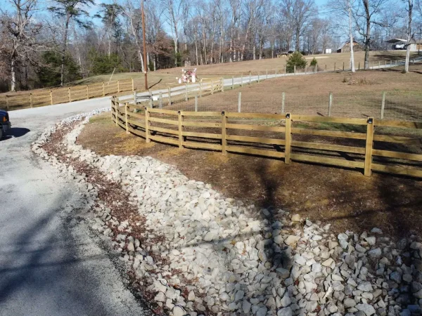 Wooden 4-board split-rail fence with natural drainage system and decorative rock along a rural driveway in Shepherdsville, Kentucky. Designed and installed by TerraCraft Outdoor Solutions to enhance property boundaries and improve stormwater management.